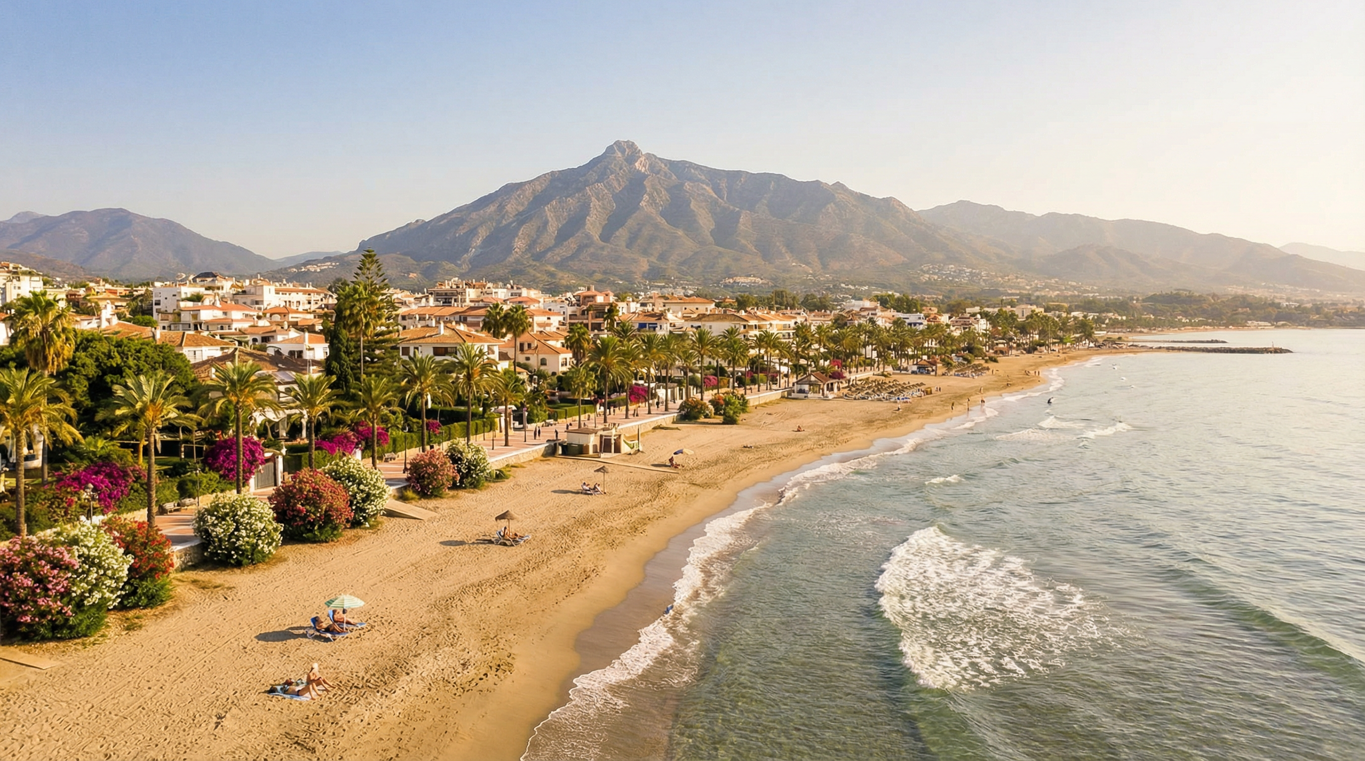 Breathtaking view of Costa del Sol with golden sandy beaches, Sierra Blanca mountains, and sunbathers in Marbella, Spain under warm Mediterranean sunlight.