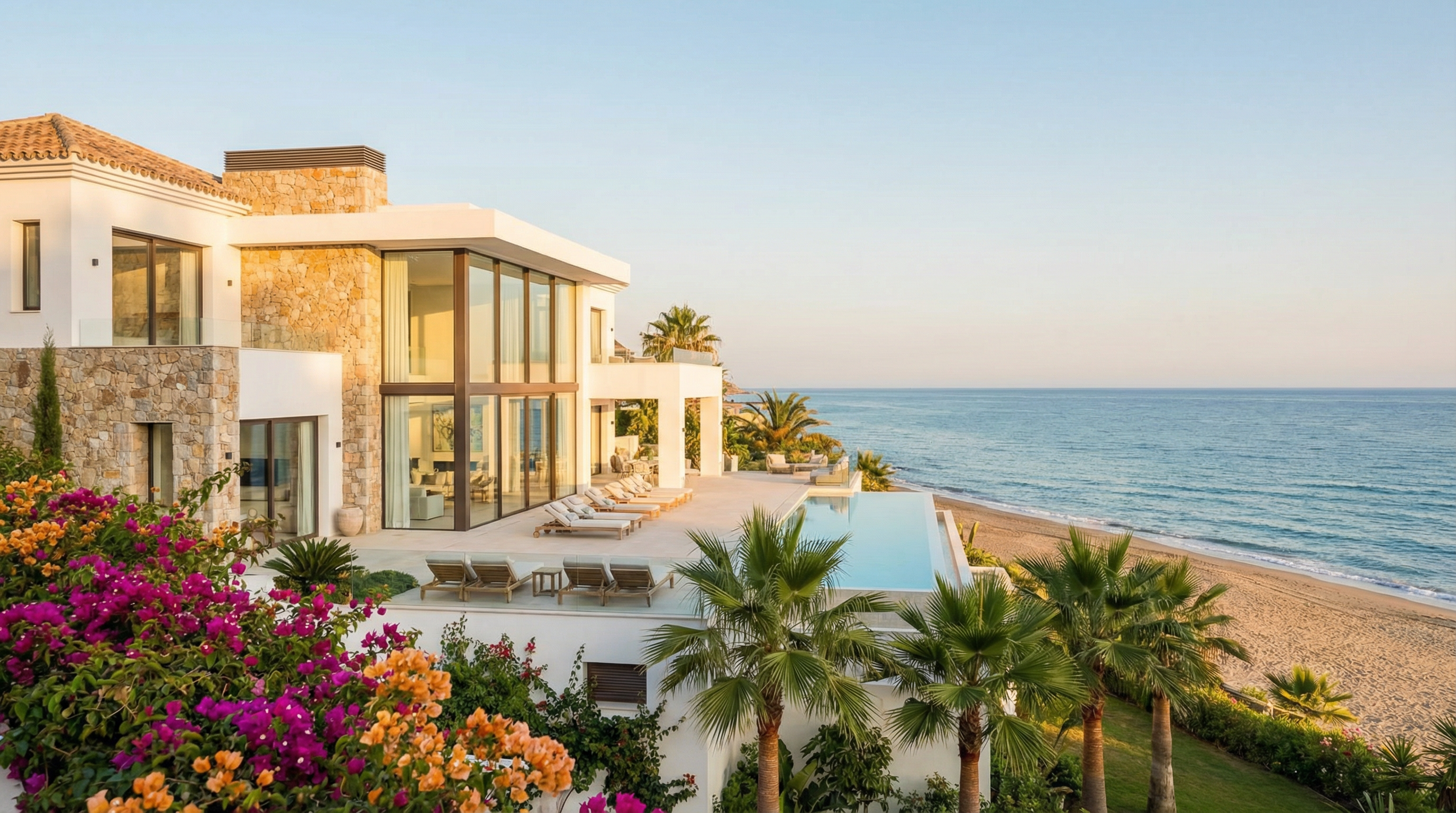 Nowoczesna nieruchomość przy plaży na Costa del Sol z dużymi szklanymi oknami, przestronnym tarasem i żywą bougainvilleą, prezentująca architekturę śródziemnomorską.
