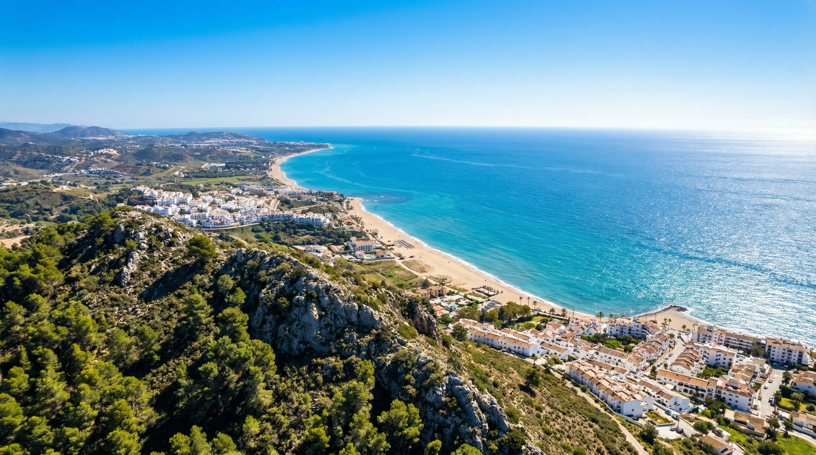 Luchtfoto van de kustlijn van de Costa del Sol met levendige mediterrane wateren, zandstranden en de Sierra de Mijas bergen onder een heldere blauwe lucht.